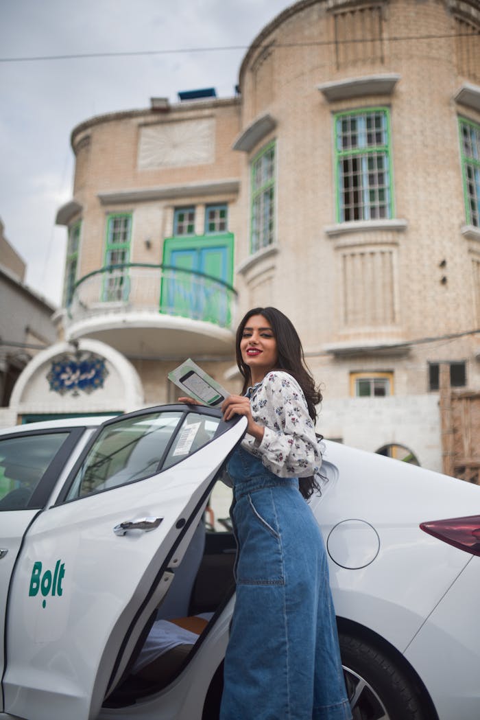 Young woman standing beside a Bolt car, holding her phone, and smiling.